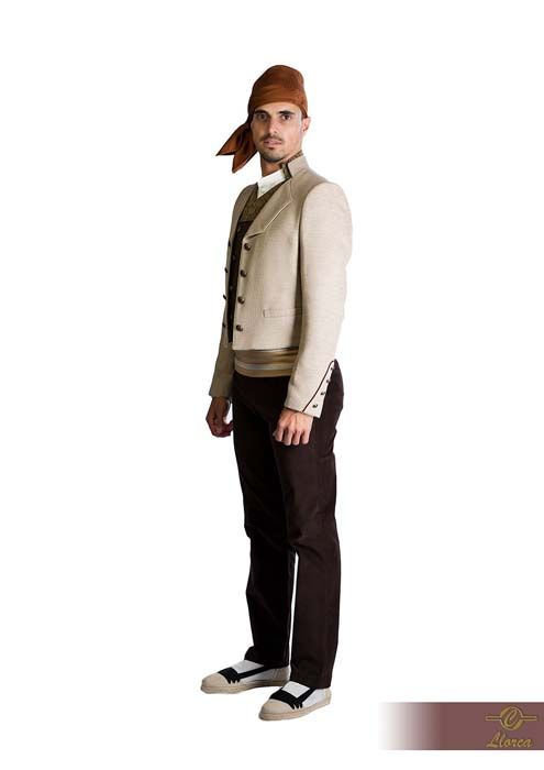 Una persona con un atuendo tradicional catalán: pañuelo marrón en la cabeza, chaqueta beige claro, pantalones marrones y alpargatas.