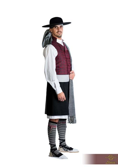 Una persona con atuendo folclórico tradicional, que incluye un sombrero negro, un chaleco color burdeos, una camisa blanca, una falda escocesa negra y calcetines estampados.