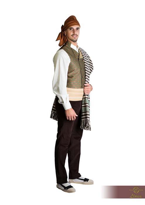 Un hombre con traje tradicional que incluye un turbante marrón, un chaleco estampado, una camisa blanca, una faja y un chal a rayas.