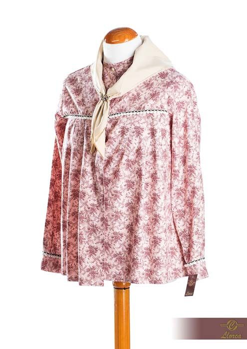 Una blusa de manga larga con estampado floral rosa y blanco y un pañuelo color crema al cuello, expuesta en un maniquí de madera.
