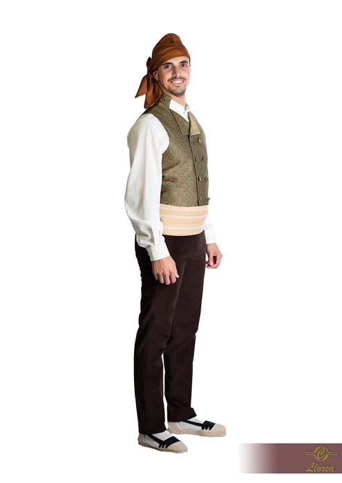 Una persona que lleva un turbante marrón, camisa blanca, chaleco verde oliva estampado, faja clara, pantalones oscuros y zapatos tradicionales.