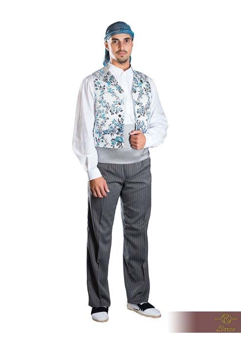 Una persona que viste un atuendo tradicional compuesto por una camisa blanca abotonada, un chaleco azul claro con estampado floral, pantalones grises y un pañuelo en la cabeza.