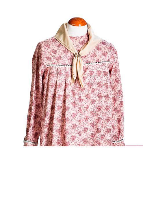 Un maniquí exhibe una blusa de manga larga con estampado floral rosa y blanco, y una bufanda lisa de color crema en el cuello.