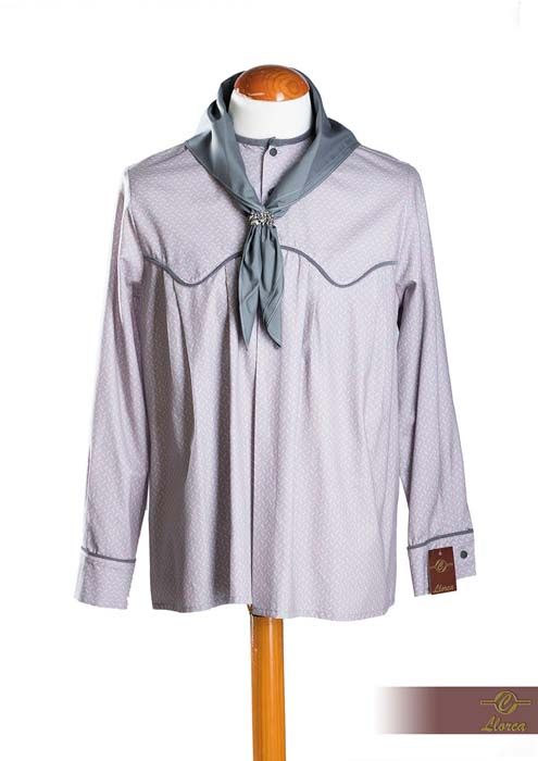 Una camisa de manga larga de color lila claro con ribetes grises y un pañuelo gris al cuello, expuestas sobre el torso de un maniquí de madera.