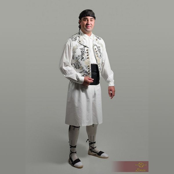 Una persona que viste un traje folclórico tradicional que consiste en una camisa blanca, un chaleco estampado, una falda, polainas y alpargatas.