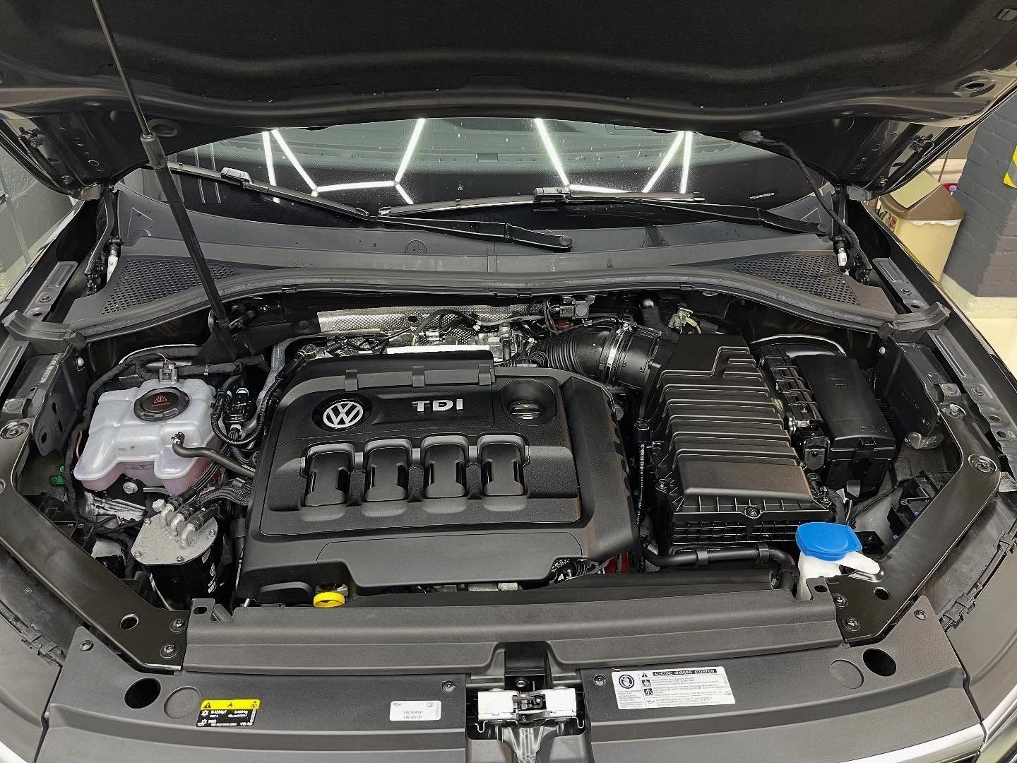 Der geöffnete Motorraum eines modernen Volkswagen TDI Dieselfahrzeugs, der den Motorblock, den Kühlmittelbehälter und das Gehäuse zeigt.