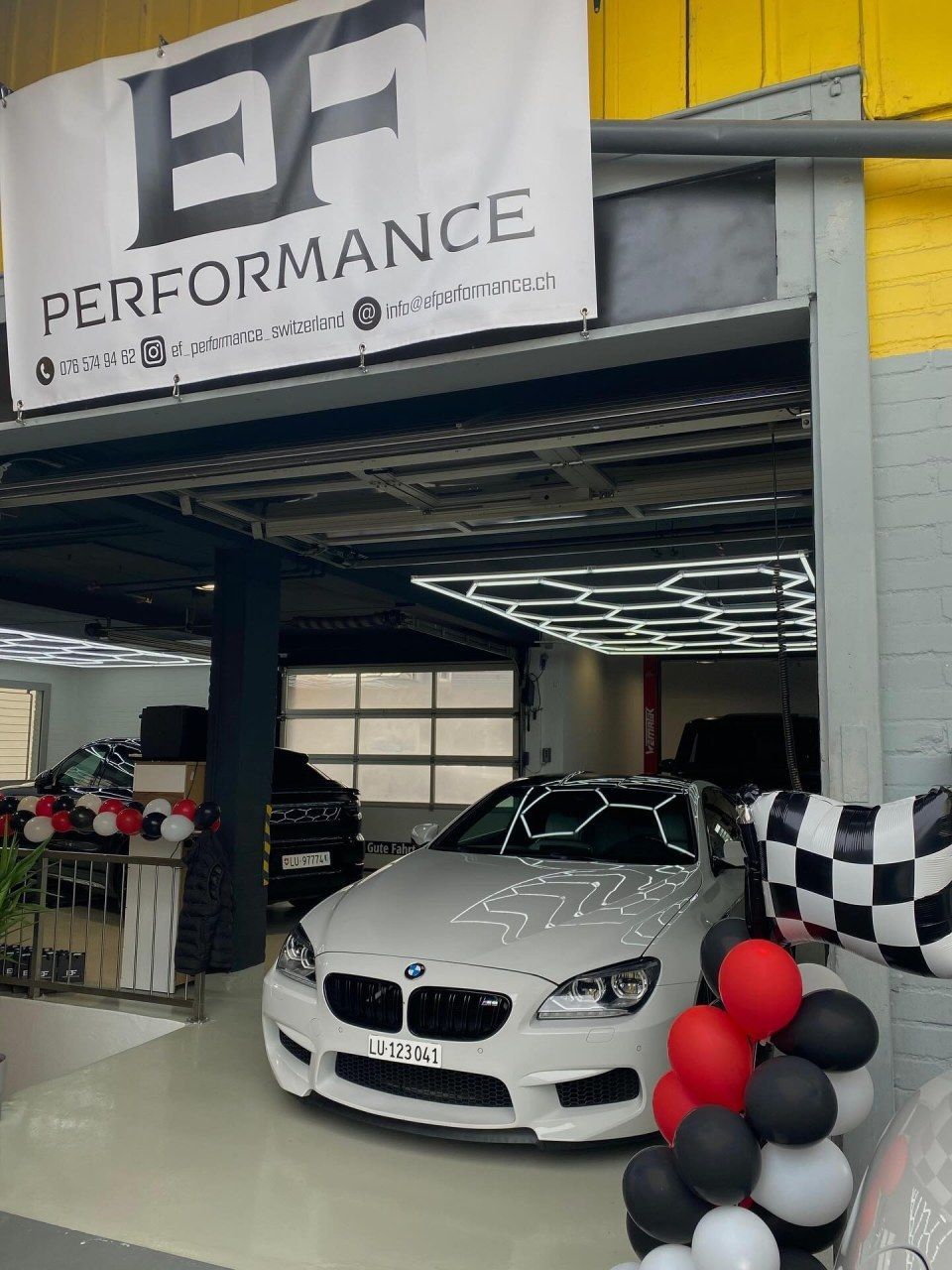Ein weisser BMW parkte in einer Garage mit der Aufschrift „EF Performance“, die mit roten, weissen und schwarzen Luftballons geschmückt war.