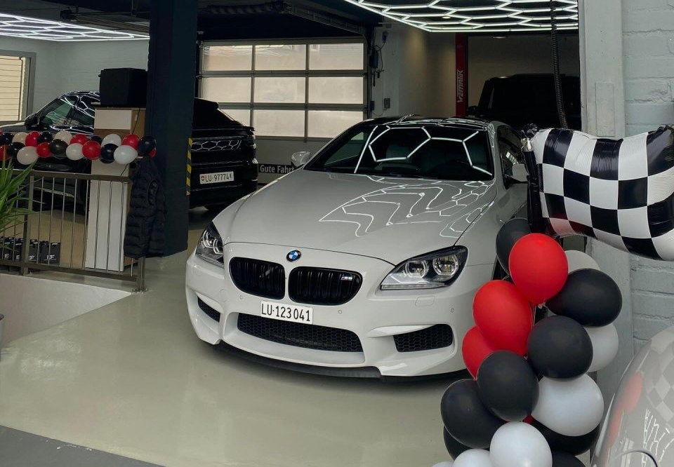 Ein weisser BMW parkte in einer Garage mit der Aufschrift „EF Performance“, die mit roten, weissen und schwarzen Luftballons geschmückt war.