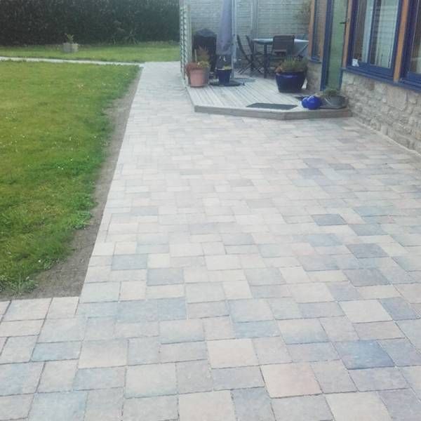 Patio en pierre au bord d’une pelouse menant à une maison, avec des plantes en pot et du mobilier de jardin