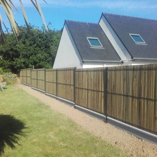Clôture en bois occultante le long d’un jardin enherbé, à côté de maisons modernes aux toits gris foncé.
