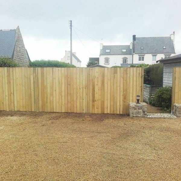 Clôture de jardin en bois, cour gravillonnée, mur de pierre et maisons en arrière-plan