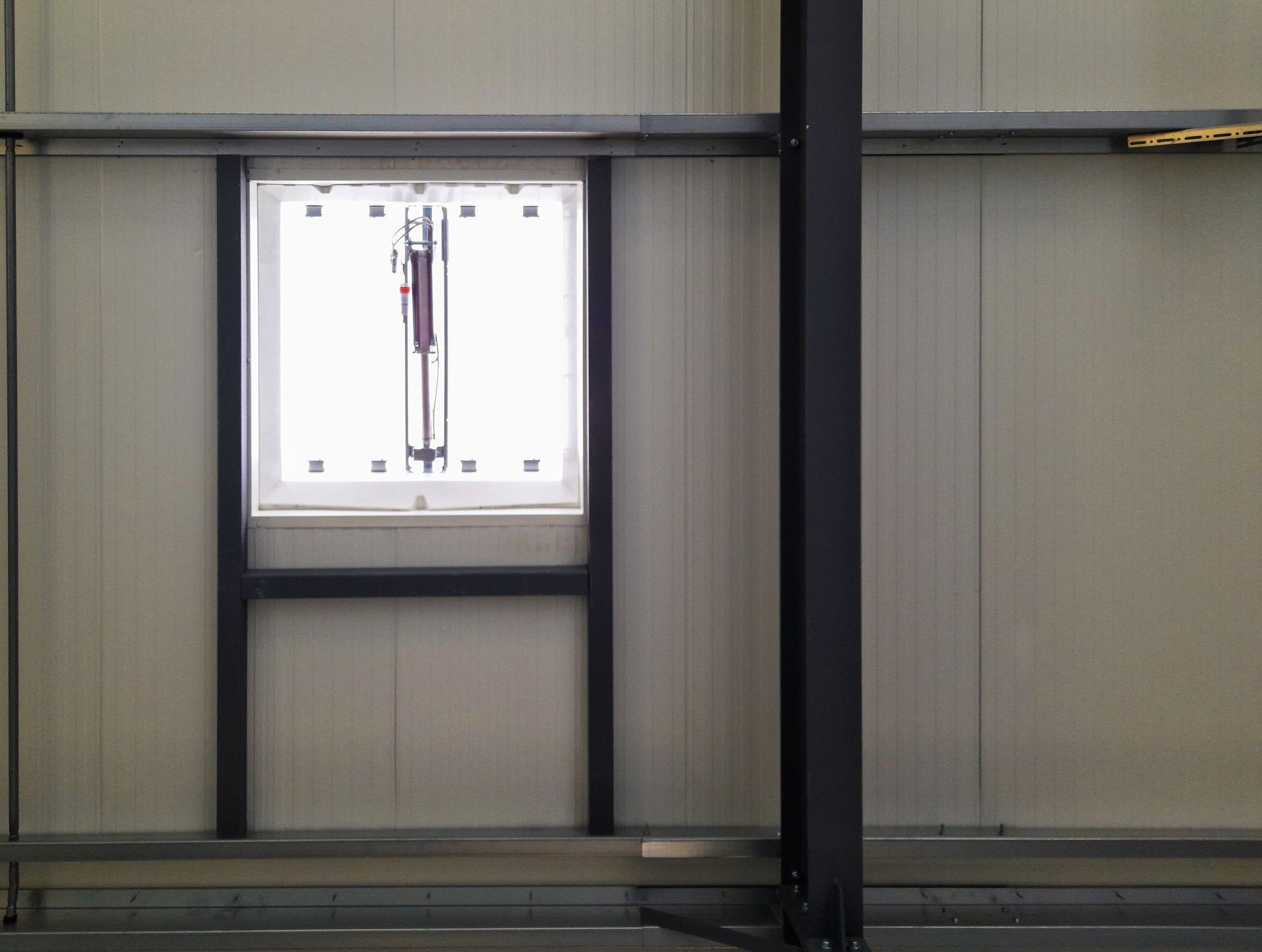 Fenêtre dans un bâtiment industriel à panneaux blancs avec un cadre en métal noir et une poutre de support.