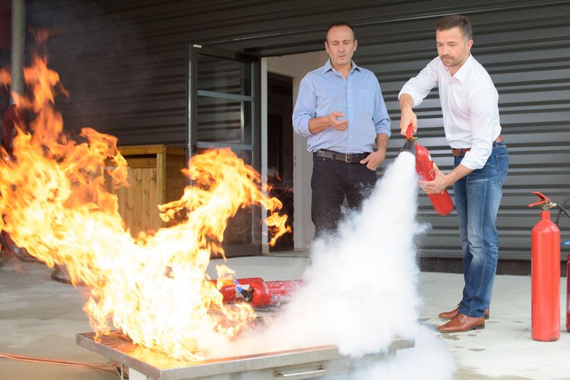 Un homme utilise un extincteur pour éteindre un incendie lors d'une séance d'entraînement ; un autre homme regarde.
