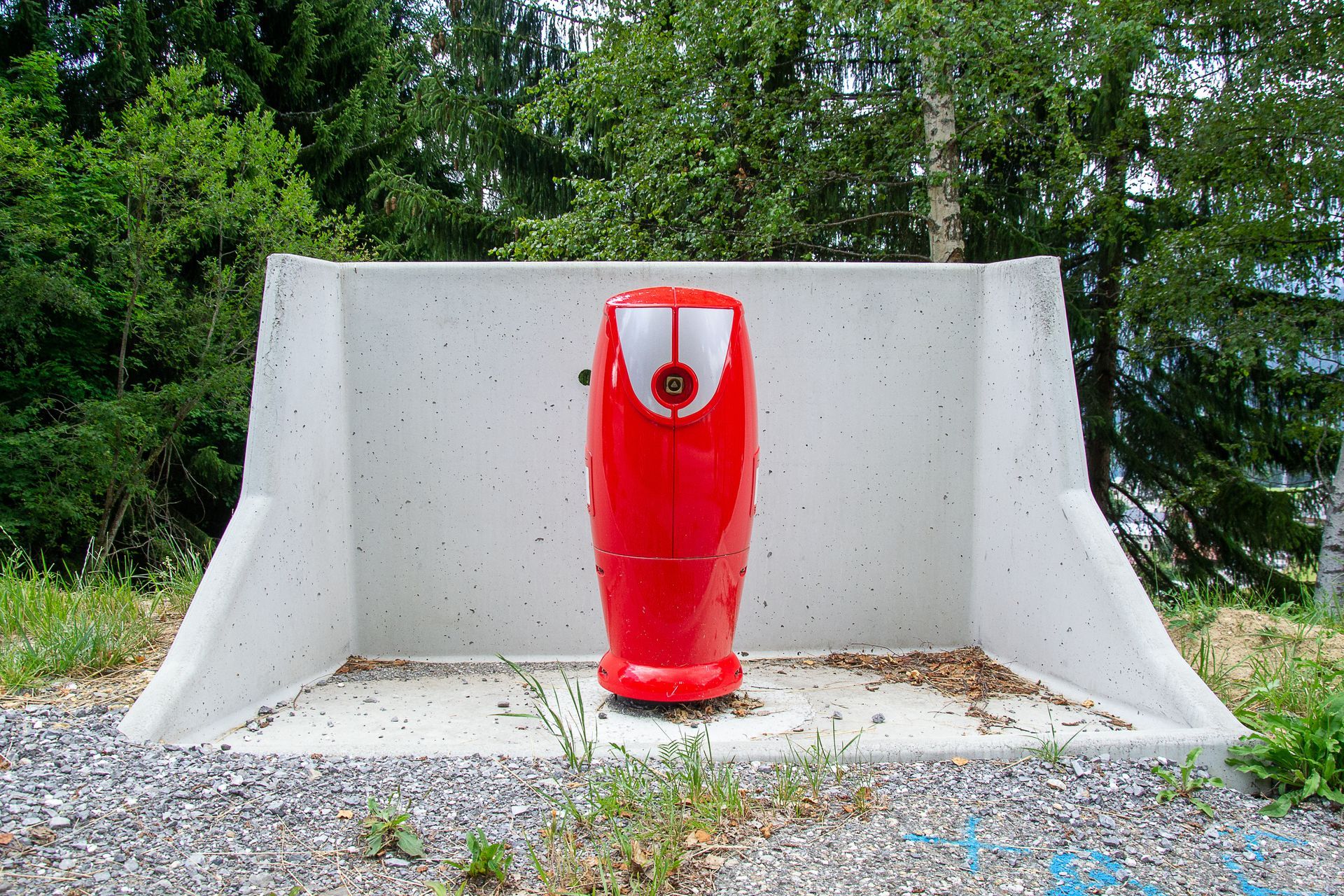 Bouche d'incendie rouge sur une base en béton dans un cadre extérieur naturel.