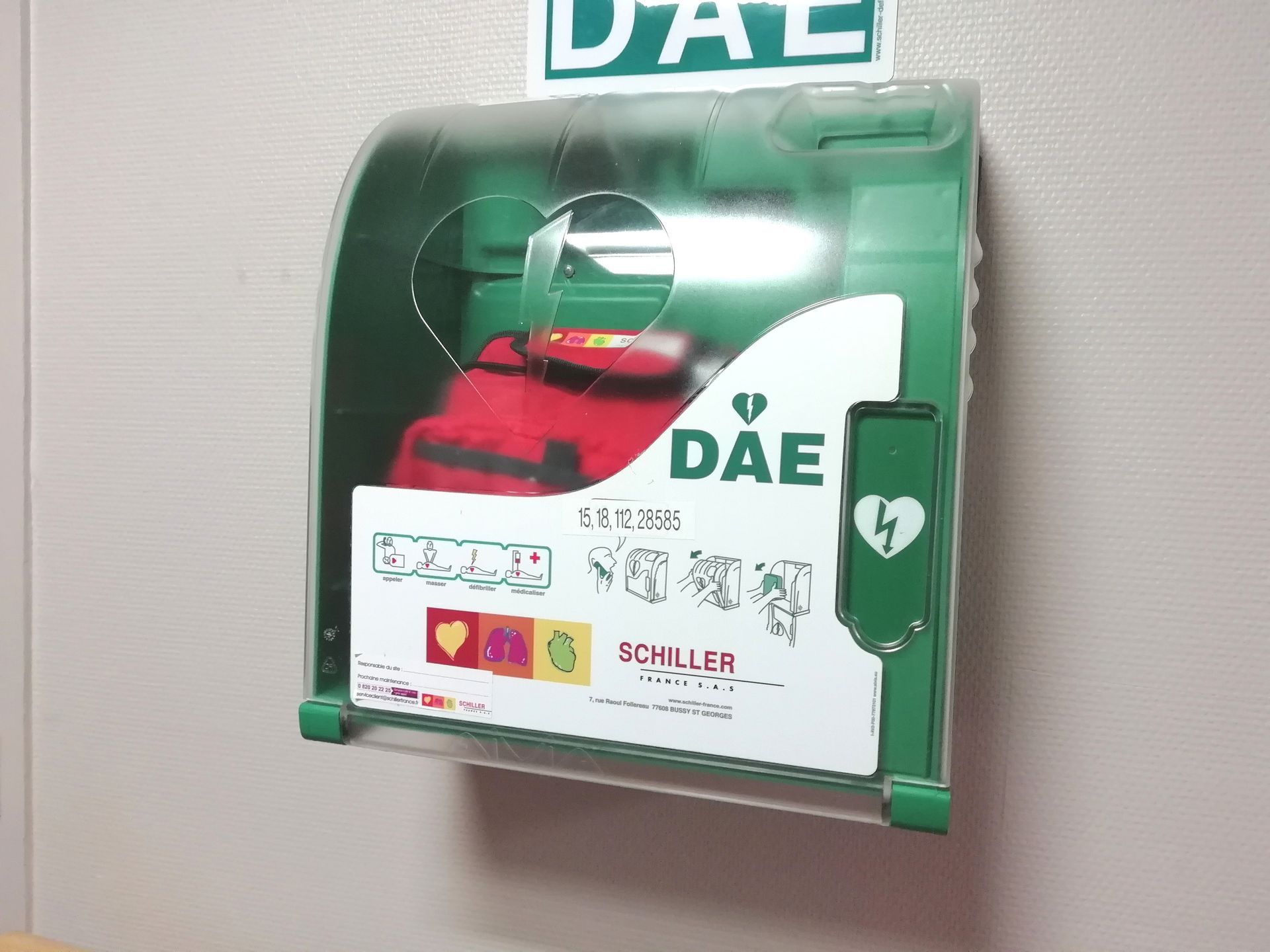 Armoire AED verte sur un mur, étiquetée « DAE ».
