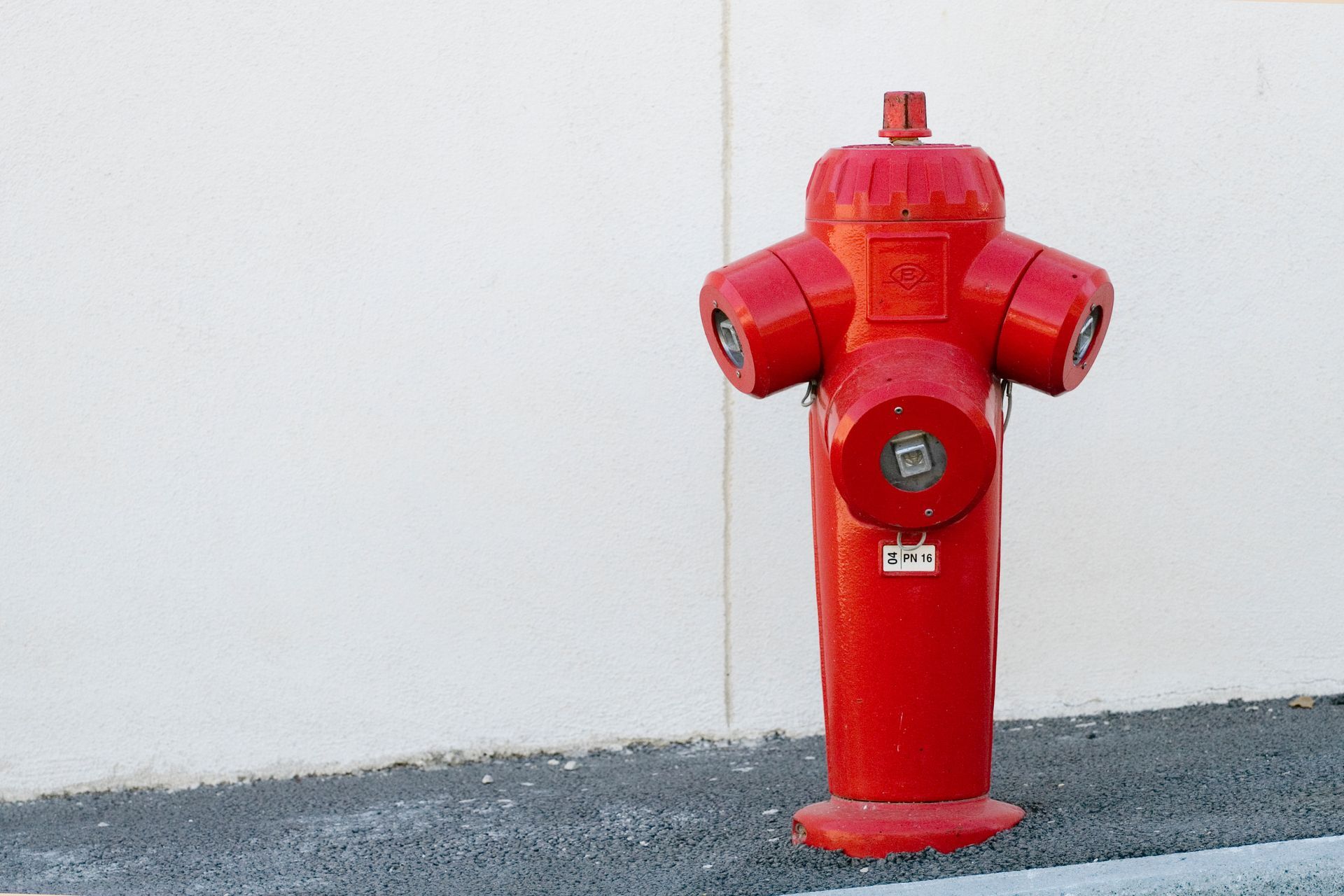 Bouche d'incendie rouge contre un mur blanc et une surface d'asphalte grise.