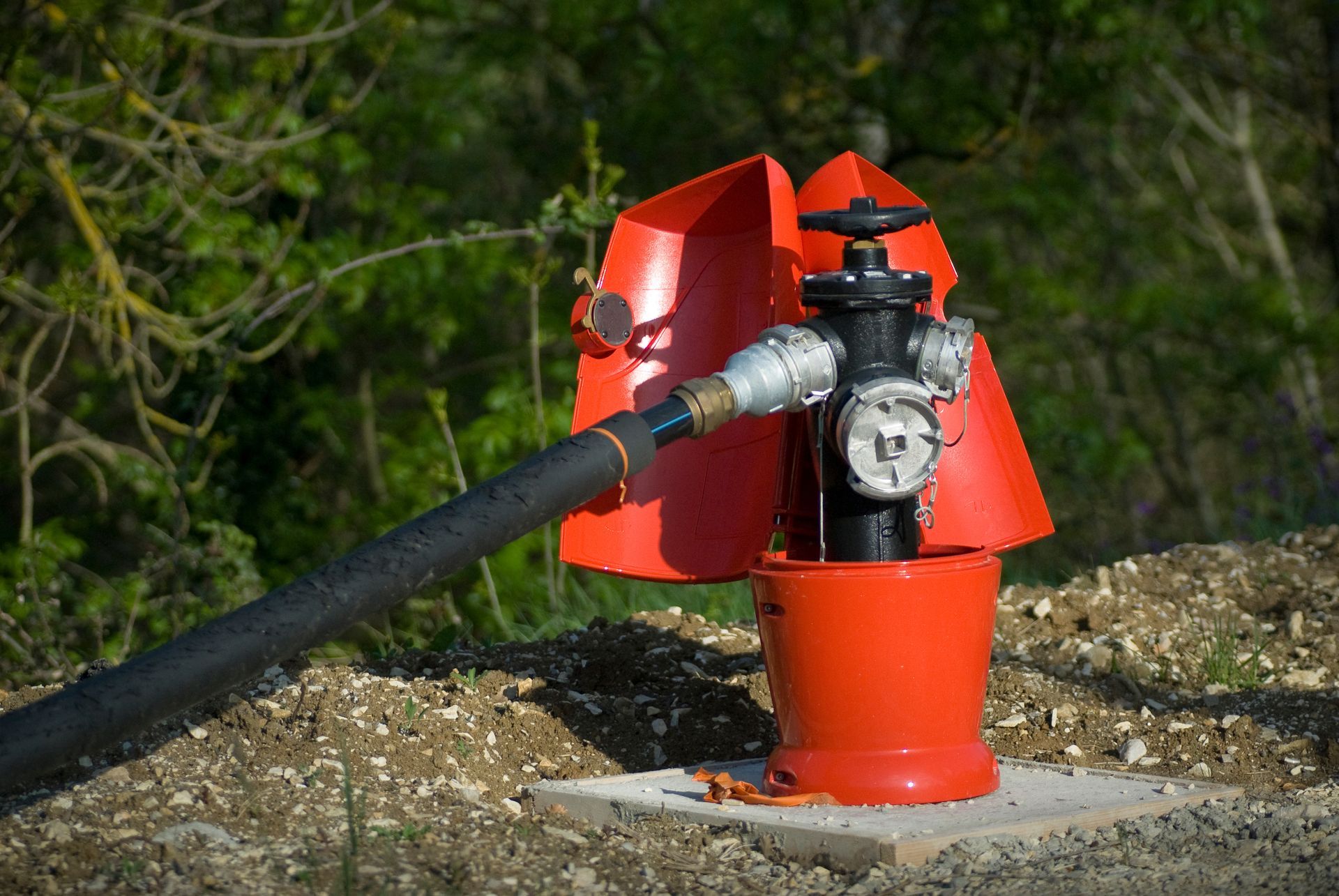 Bouche d'incendie rouge avec tuyau attaché, posée sur une base en béton dans un cadre extérieur naturel.