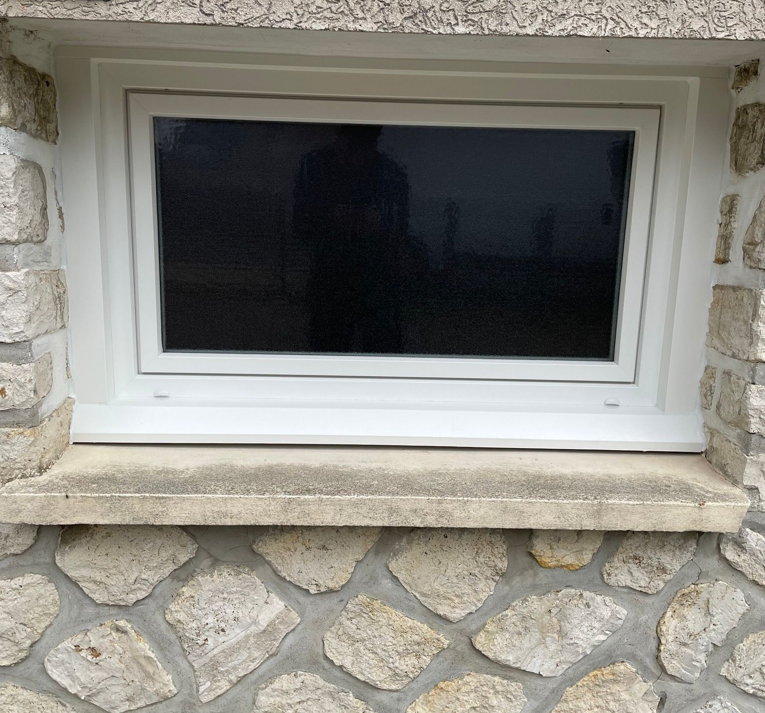 Fenêtre à cadre blanc dans un mur de pierre. Le verre est noir.