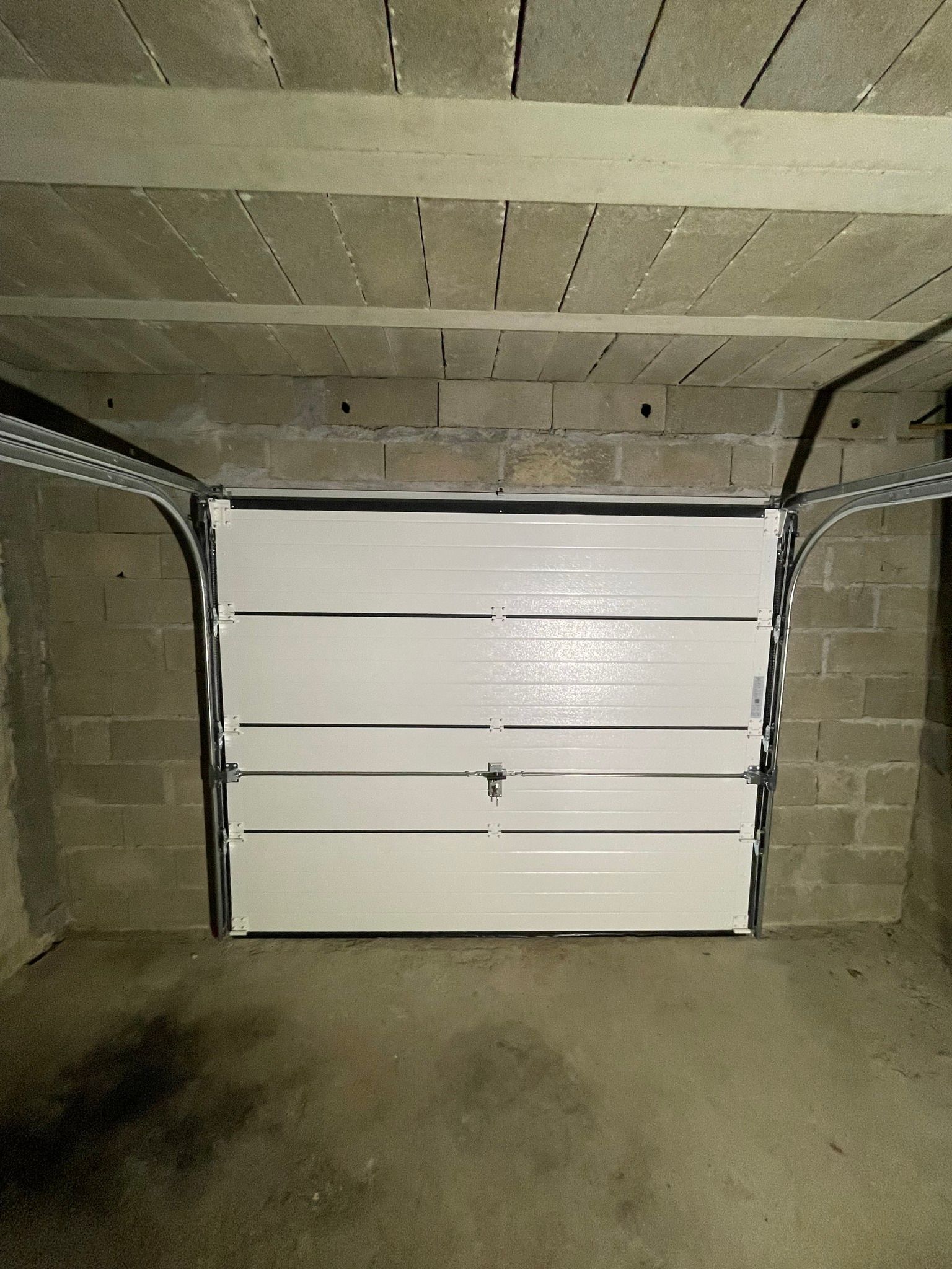 Porte de garage blanche dans un garage en parpaings.