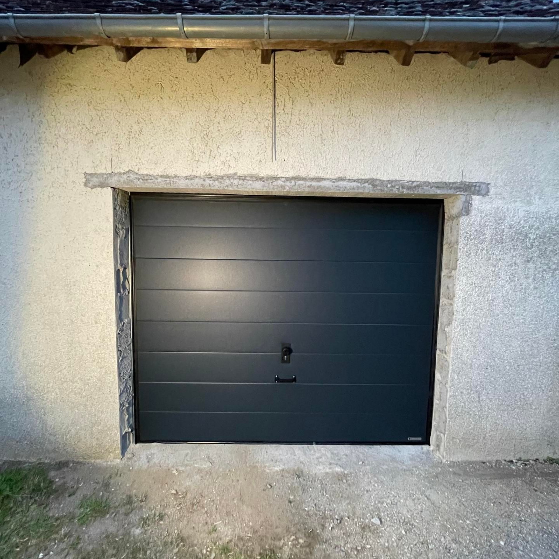 Porte de garage gris foncé sur un bâtiment en stuc clair.