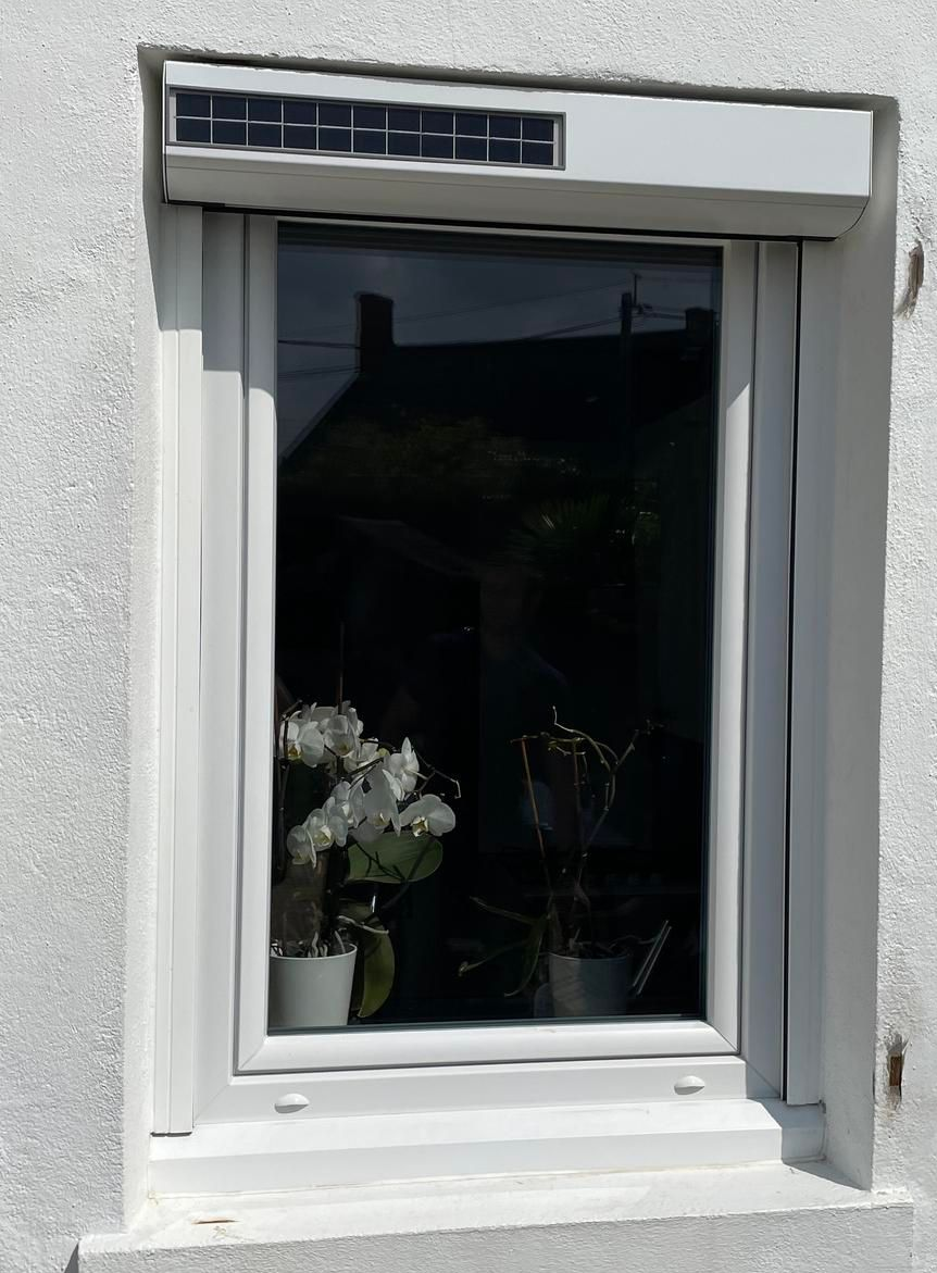 Fenêtre à volet enroulé, encadrée d'un enduit blanc texturé, encastrée dans un mur en pierre.