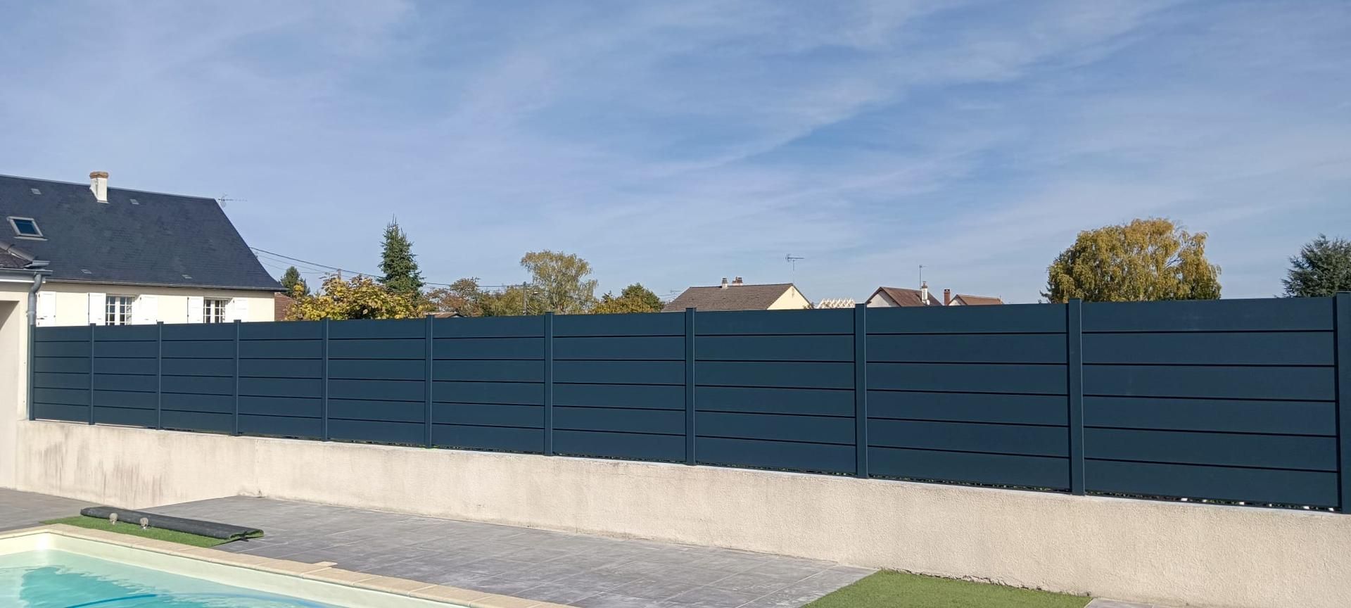 Clôture bleue le long d'un mur en béton, avec une piscine au premier plan.