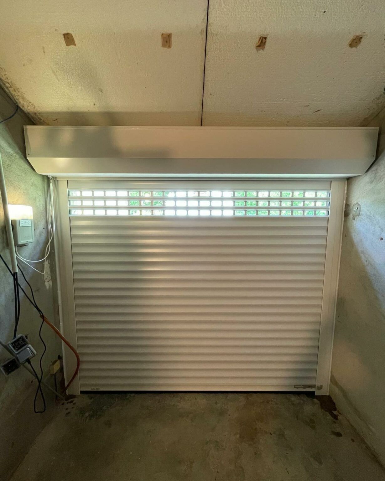 Porte de garage sectionnelle blanche fermée, avec une vitre dépolie, à l'intérieur d'un garage aux murs en béton.