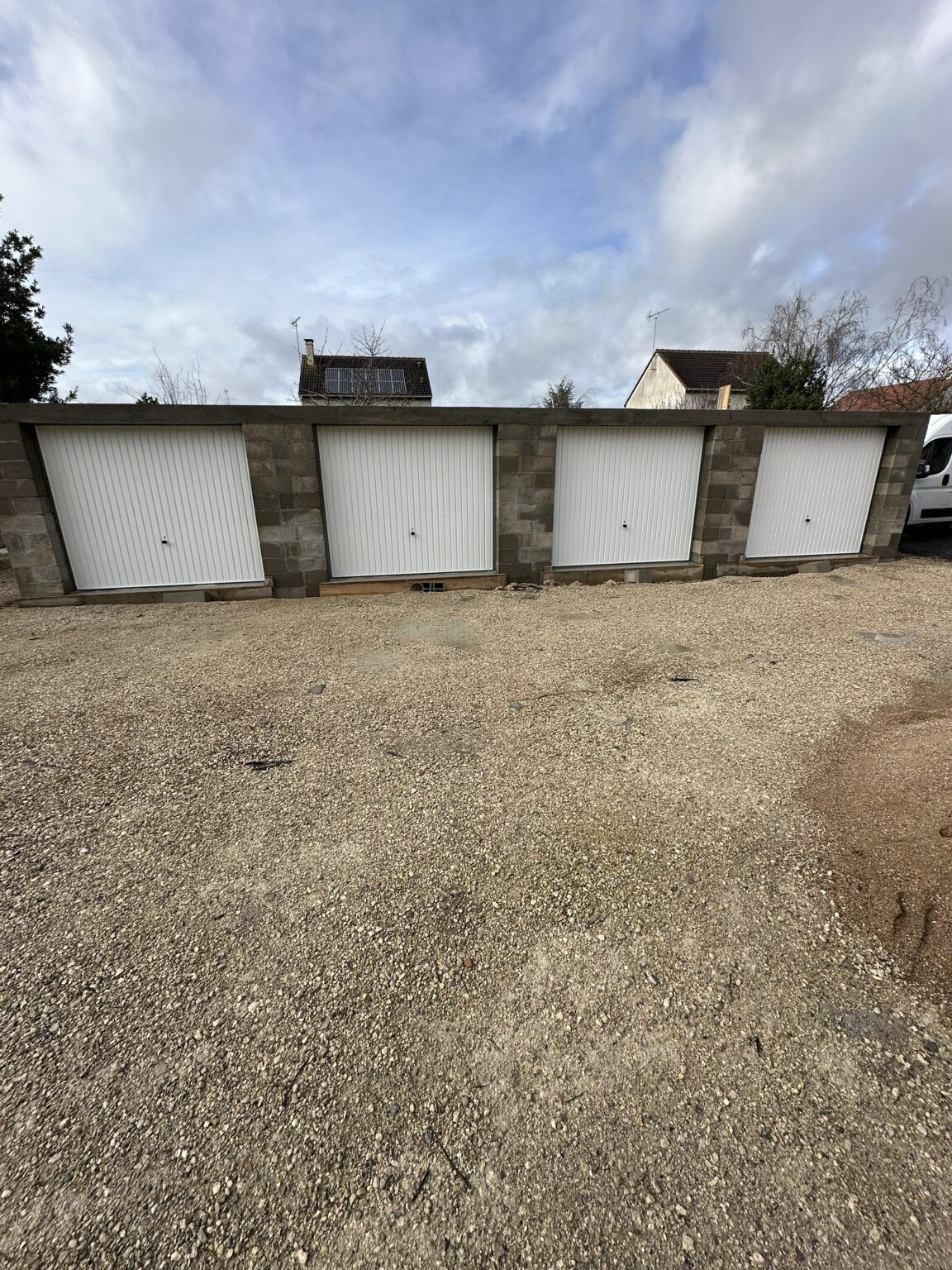 Quatre portes de garage blanches alignées, avec du gravier.