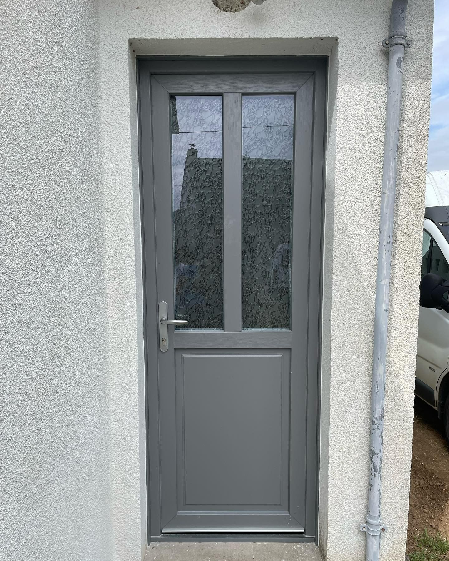 Porte grise à panneaux de verre encastrée dans un mur en stuc blanc.