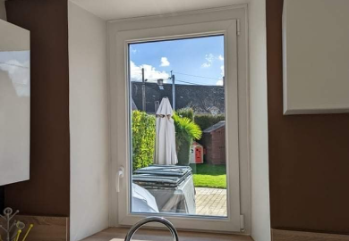Fenêtre donnant sur un jardin : parasol blanc, haie verte.