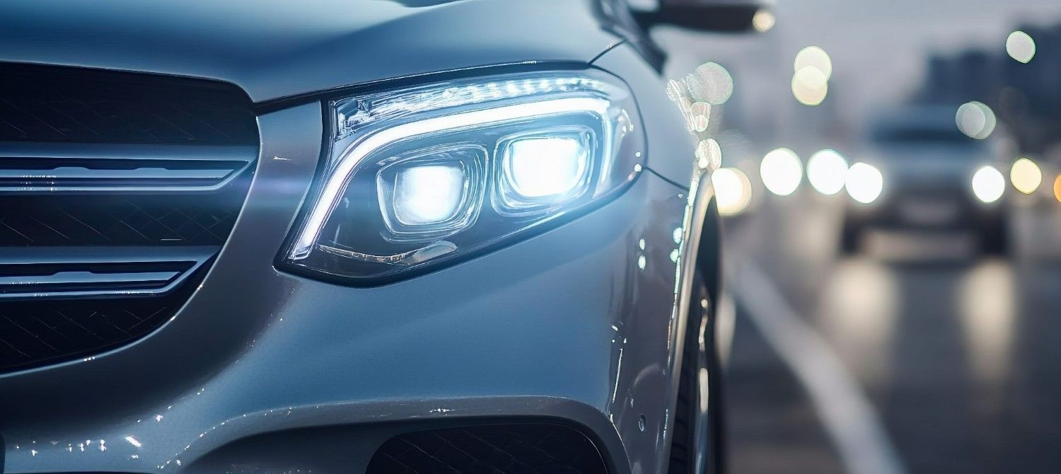 Primer plano del faro LED brillante de un coche plateado en una carretera al anochecer, con el tráfico borroso al fondo.