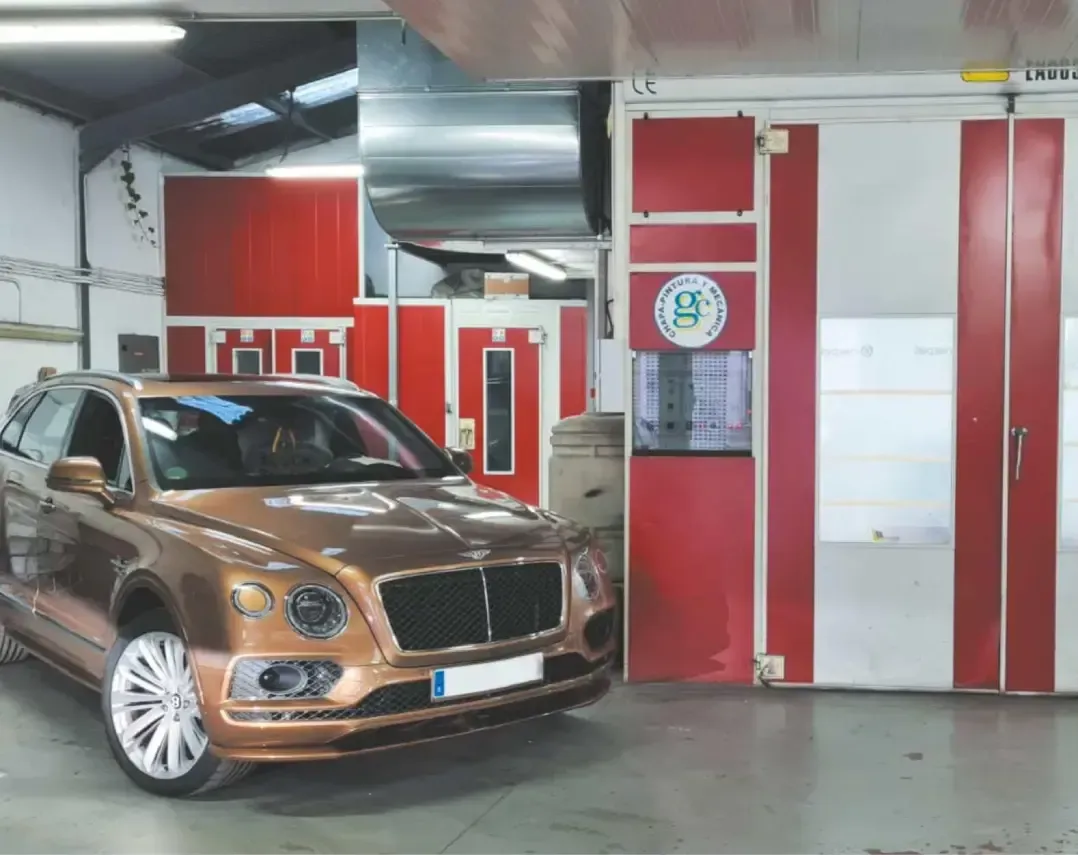 Un coche marrón está aparcado en un garaje al lado de una puerta roja.