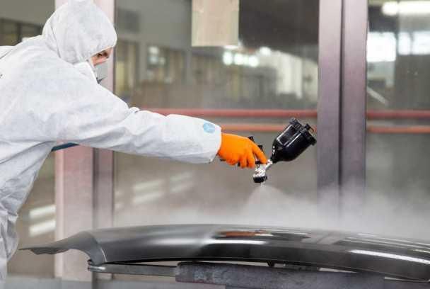 Un hombre con un traje de protección está pintando con aerosol el parachoques de un automóvil.