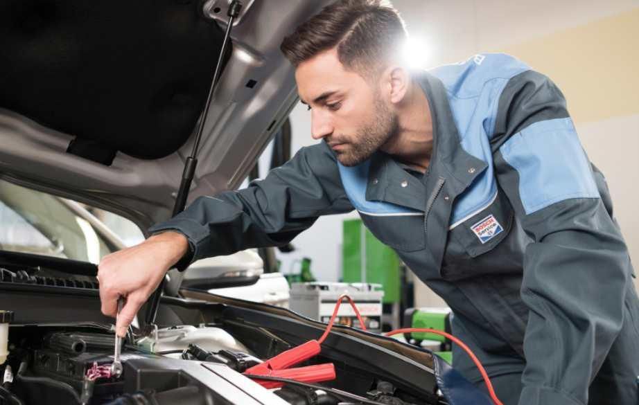 Un hombre está trabajando en un coche con el capó abierto.