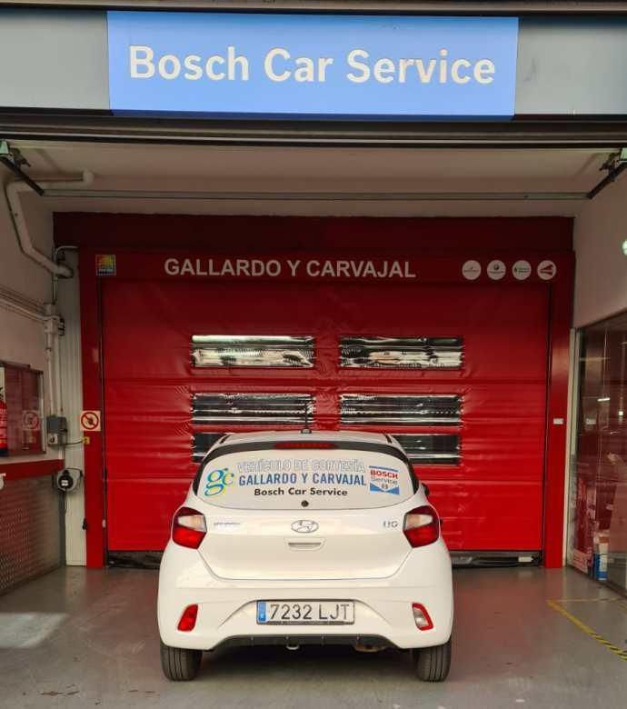 Un coche blanco está aparcado delante de un taller de servicio de automóviles Bosch.