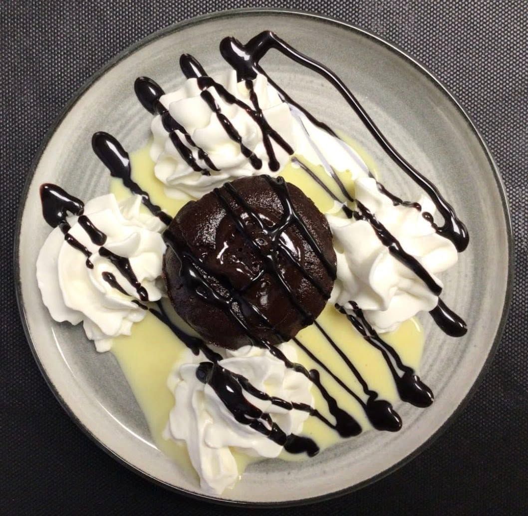 Assiette de dessert avec un gâteau au chocolat fondant, de la crème fouettée et un filet de chocolat.