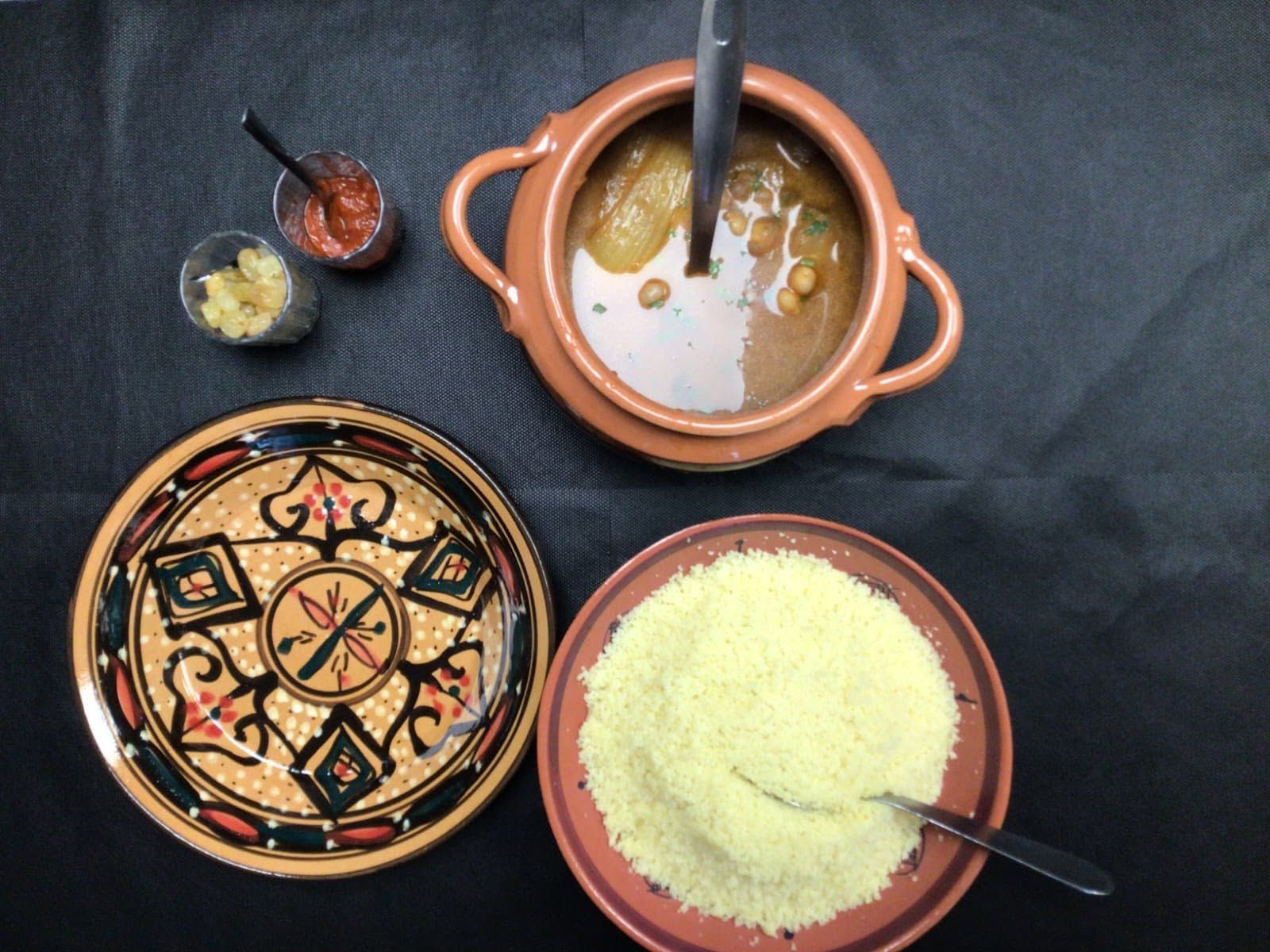 Trois plats avec des cuillères sont disposés sur une table sombre, dont un couvercle décoré et une marmite en terre cuite.