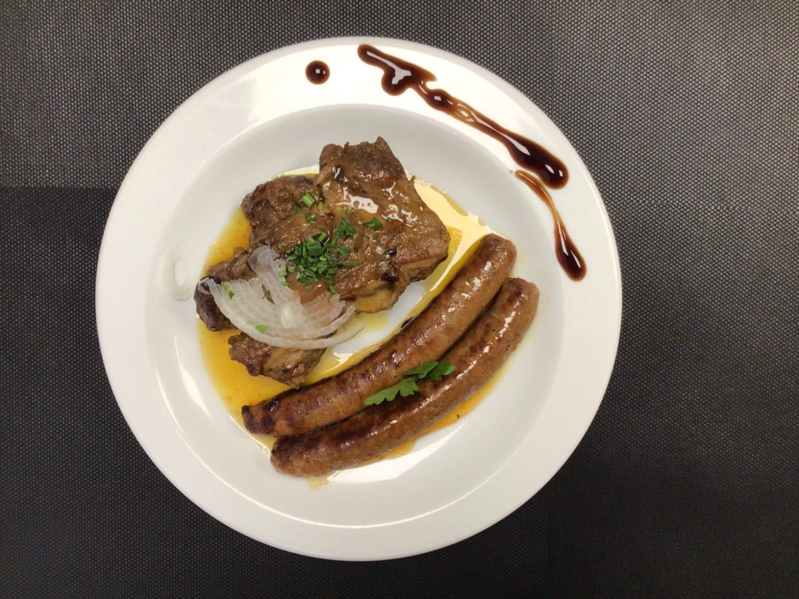 Plat gastronomique composé de saucisses, de viande, de légumes et de sauce, servi dans une assiette blanche.
