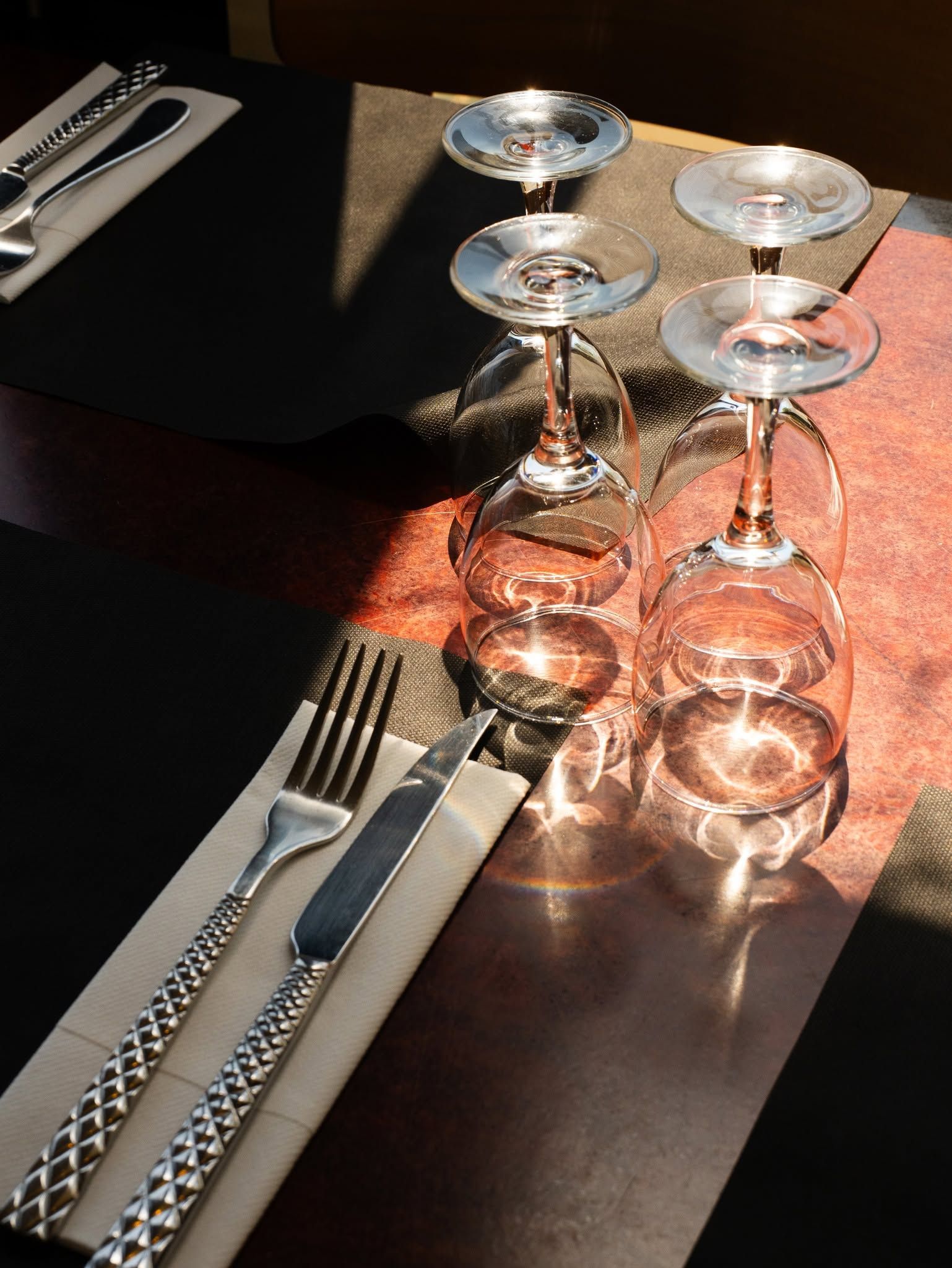 Verres à vin et couverts sur une table ensoleillée aux reflets chauds