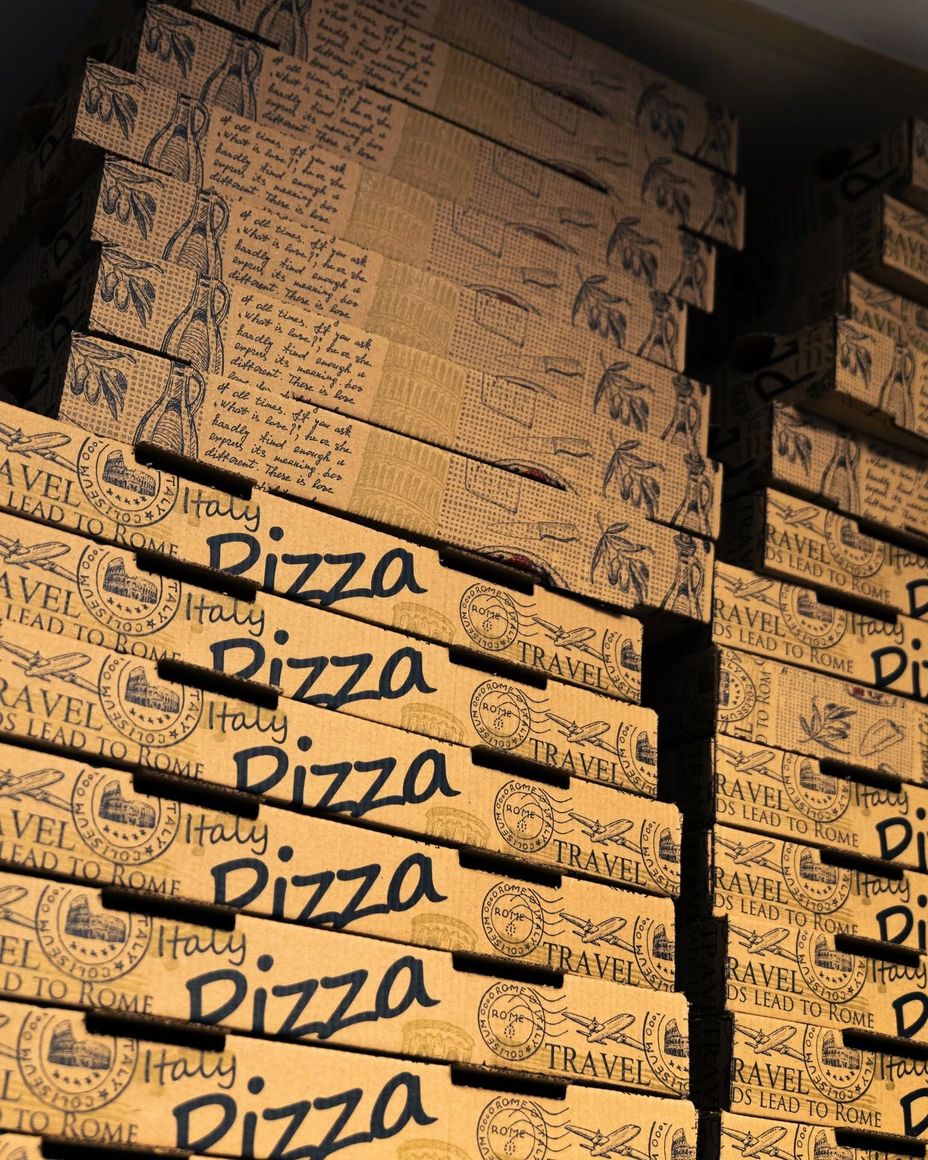 Des piles de boîtes à pizza beiges avec des inscriptions noires.