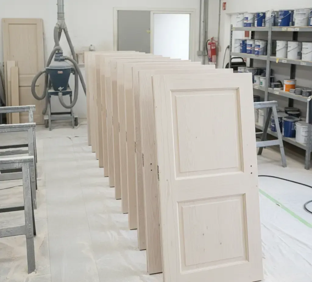 Puertas de madera lijadas y preparadas para lacar en taller.