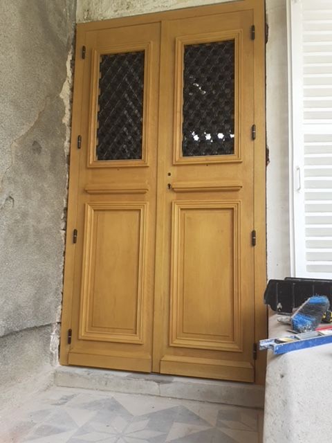 Porte d'entrée double en bois avec panneaux de verre à motif losange, encastrée dans un porche en pierre.