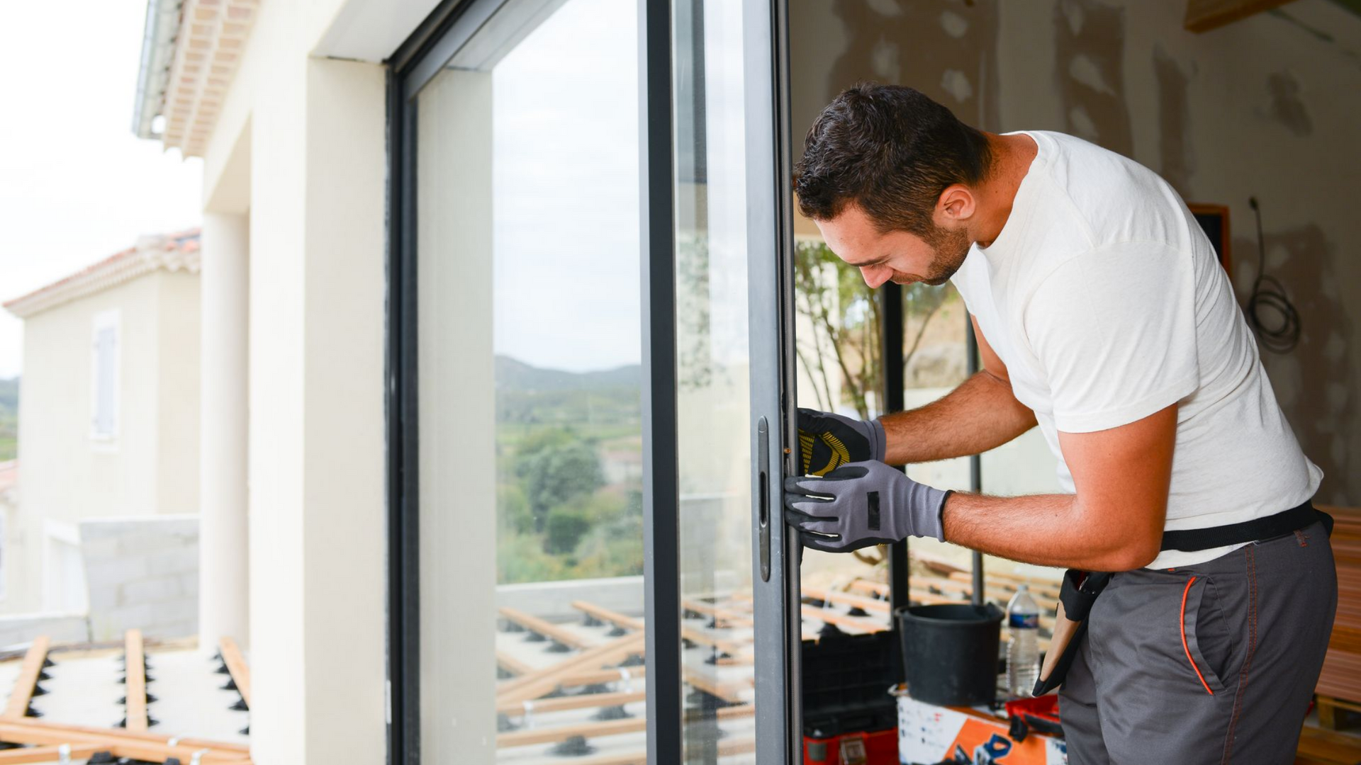 Un ouvrier en tee-shirt blanc utilise une perceuse pour installer un cadre de fenêtre intérieur.