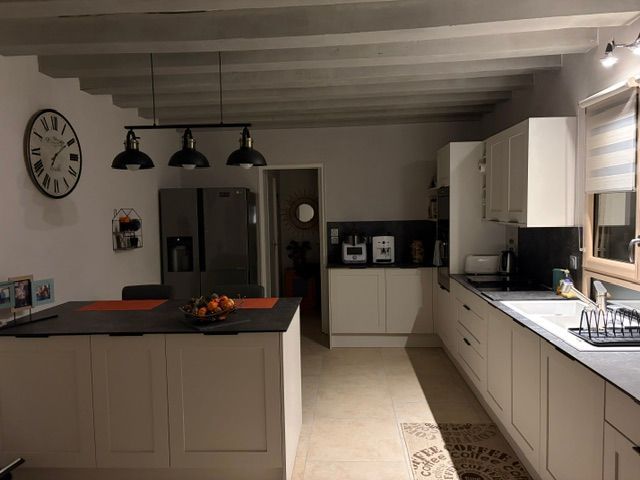 Cuisine moderne avec armoires blanches, îlot noir, suspensions lumineuses et horloge murale
