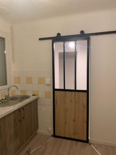 Petite cuisine avec placards en bois et porte coulissante à cadre noir donnant sur une douche carrelée