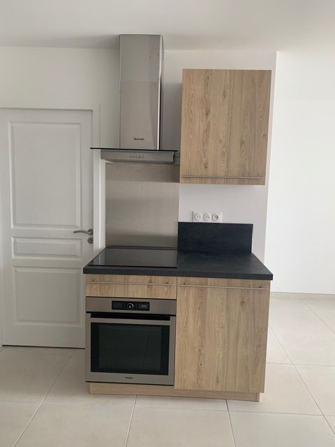 Petite cuisine moderne avec placards en bois, plan de travail noir, four et hotte en inox.