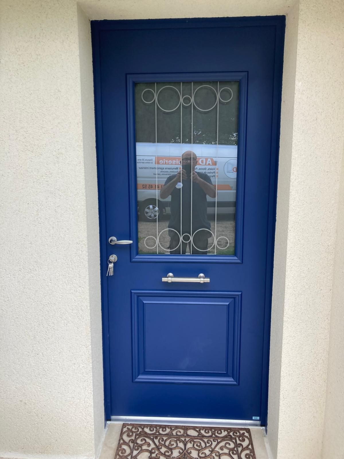 Porte d'entrée bleue avec fenêtre décorative et poignée argentée sur un mur extérieur beige