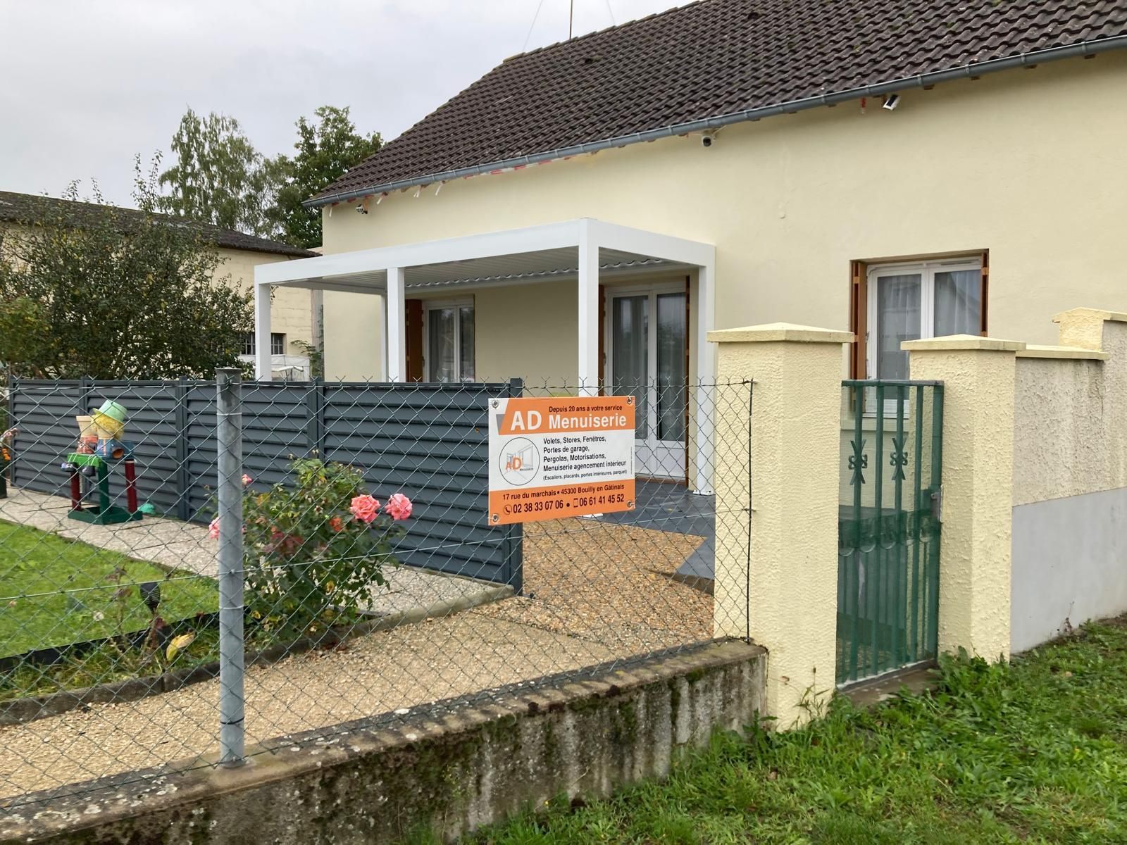 Maison avec porche et portail ouvert, avec un panneau orange « À vendre » dans la cour avant.