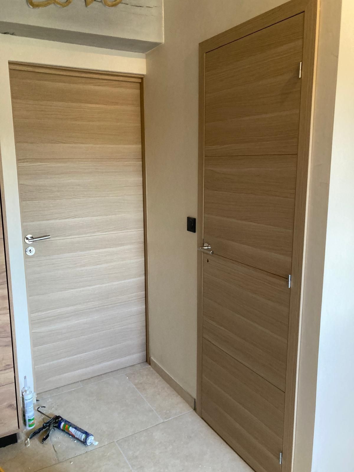 Couloir avec deux portes en bois fermées et un sol carrelé clair