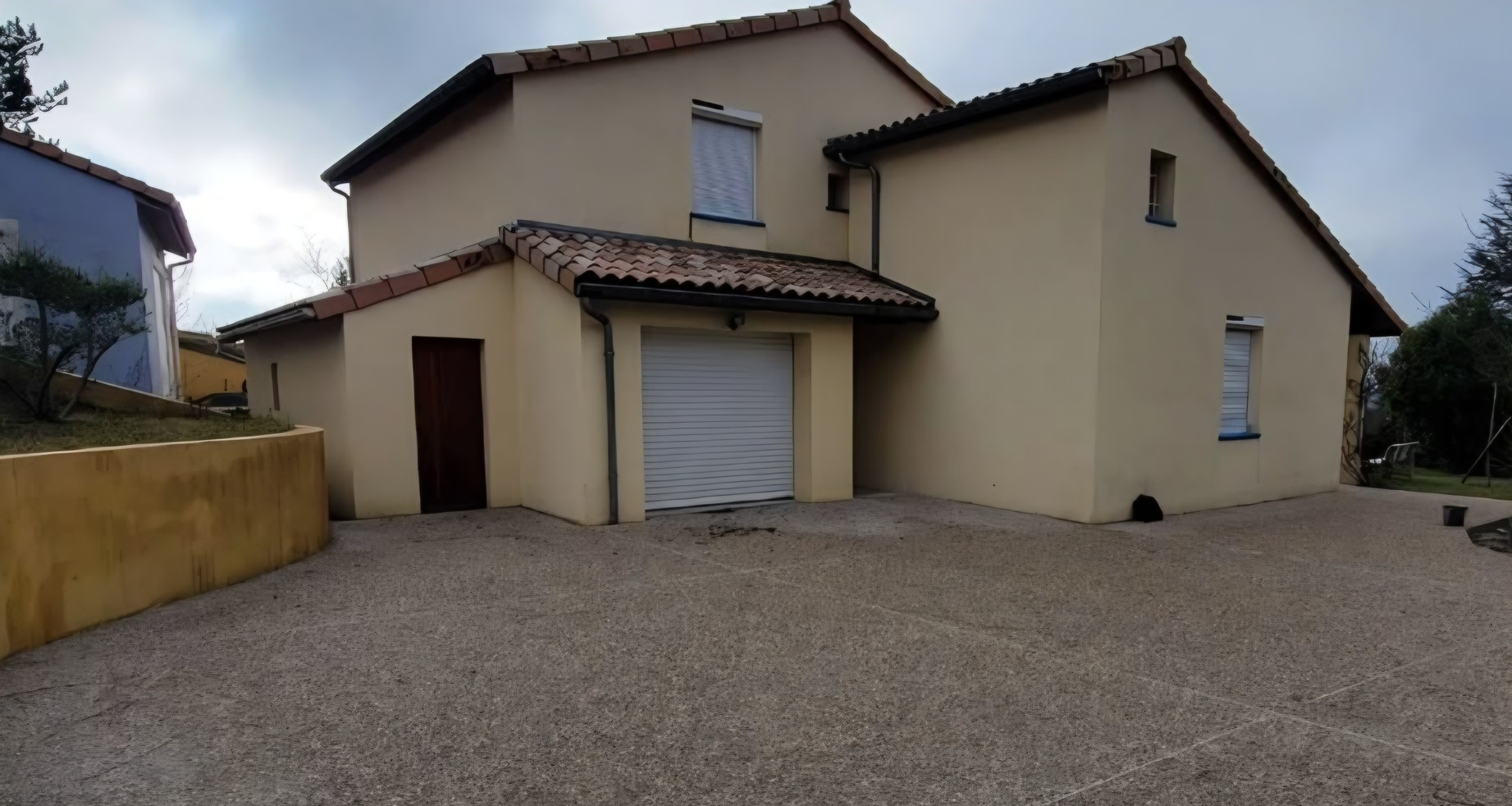 Maison à deux étages avec extérieur beige et allée en gravier.